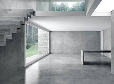 Minimalist concrete interior with floating staircase, floor-to-ceiling windows, and views of lush greenery.