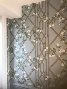 Blue trellis wallpaper with beige lattice, green leaves, and white flowers in a softly lit corner.