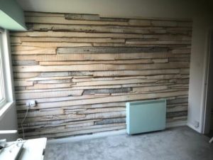 Modern rustic room with wooden plank accent wall, pastel heater, grey carpet, and natural light.