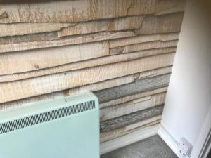 Rustic wood-effect wallpaper with green electric heater, white trim, and grey carpet in modern room.