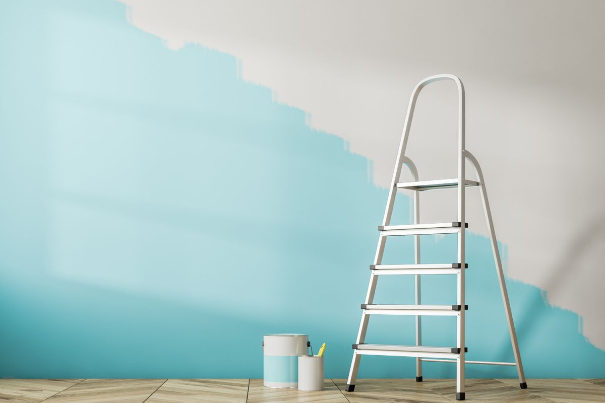 Metal step ladder and blue paint can in a modern room with a half-painted blue wall.