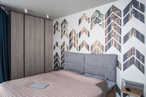 Modern bedroom with chevron pine print accent wall, large bed, wooden nightstands, and minimalist decor.