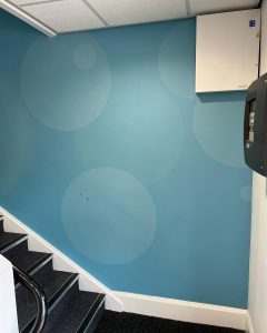 Stairwell with light blue circular pattern wall, dark carpet, white trim, and visible utility boxes.