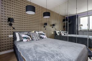 Modern bedroom with gold geometric wall, grey bedding, stylish lighting, mirrors and large window.
