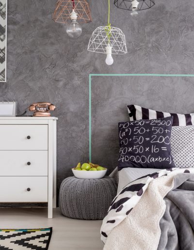 Modern grey bedroom with venetian plaster wall, geometric decor, minimalist commode, and patterned bedding.