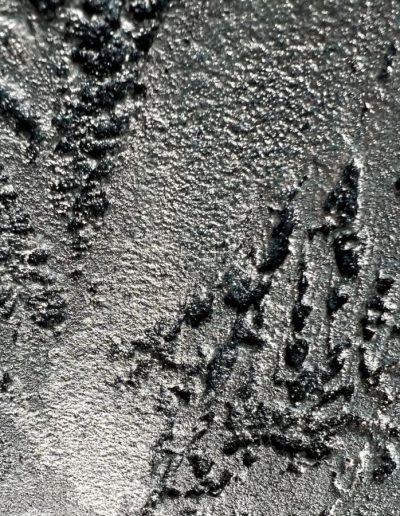 Close-up of rough, silvery metallic texture with ridges, craters, and reflective highlights.