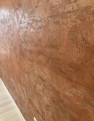 Close-up of textured Venetian plaster wall in warm earth tones with light wood flooring and white outlets.