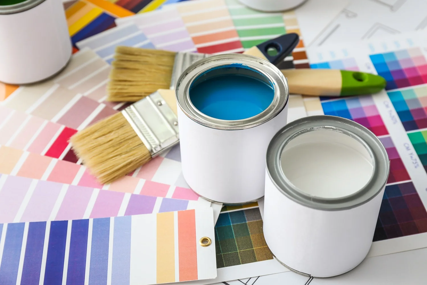 Open blue and white paint cans with brushes and colourful swatches for creative interior design choices.