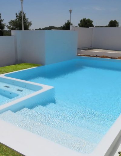 Contemporary private swimming pool with built-in jacuzzi in a sunlit, secluded garden with green lawn.