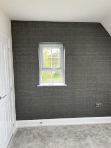 Modern grey accent wall with white window, garden view, panelled door, and light grey carpet.