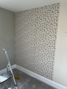 Modern accent wall with taupe wavy wallpaper, sage-grey paint, and step ladder during room renovation.