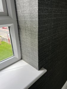 White window sill and frame beside dark textured wallpaper, with natural light and blurred outdoor scene.