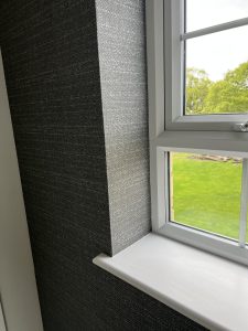 White-framed window in dark-walled room overlooking green garden, letting in soft natural light.