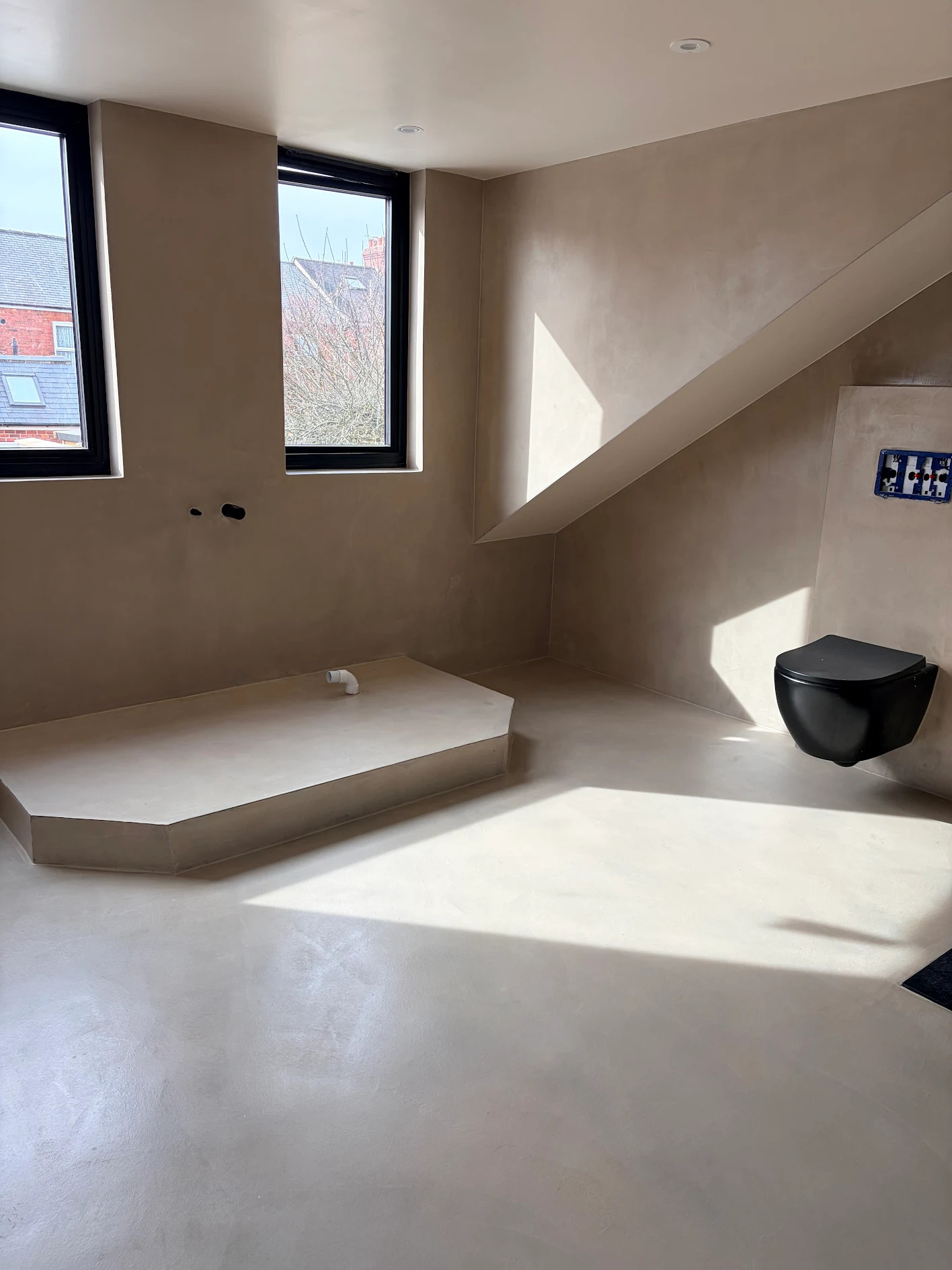Minimalist bathroom with microcement finish and a black floating toilet under a sloped ceiling